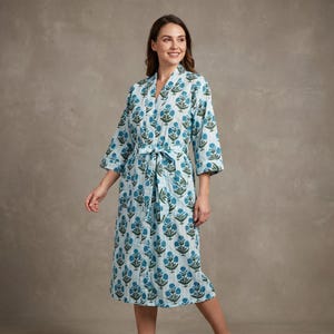 May include: A light blue robe featuring a repeating pattern of dark green and blue floral motifs. The garment has three-quarter length sleeves, a V-neckline, and a matching fabric tie belt at the waist to secure the front closure of the robe.