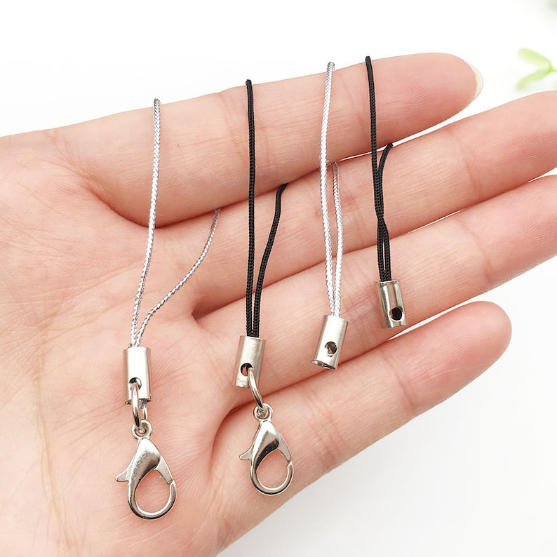 Op de afbeelding: Drie zilveren en zwarte lanyards met zilveren karabijnhaken en zilveren tonvormige eindkappen. De lanyards zijn gemaakt van een dun, gevlochten koord.