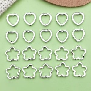 Könnte beinhalten: Silberfarbene Metallanhänger in Herz- und Sternform, angeordnet auf einer hellgrünen Oberfläche. Die Anhänger sind hohl und haben eine glatte Oberfläche. Die Herzen sind in zwei Reihen angeordnet, die Sterne darunter. Geeignet für die Schmuckherstellung.