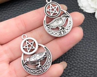 May include: Two silver-toned metal charms. Each charm features a raven inside a crescent moon with Celtic knotwork, and a pentagram. The charms have a loop at the top for attaching to jewelry or other crafts.