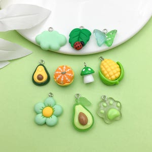 Puede incluir: Surtido de dijes de arcilla verde, amarillo, naranja y rojo con varias formas, incluyendo una nube, una hoja, una mariposa, un aguacate, una naranja, un hongo, maíz, una flor y una huella de pata.