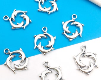 May include: Seven silver-toned dolphin charms, each featuring three dolphins swimming in a circle. The charms are perfect for jewelry making or crafting projects.