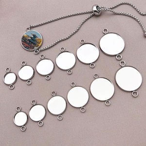 Puede incluir: Una colección de bases de pulseras y colgantes de metal plateado. La pulsera presenta un dije redondo con una imagen colorida de un edificio. Se muestran varios tamaños de bases redondas, cada una con pequeños bucles.