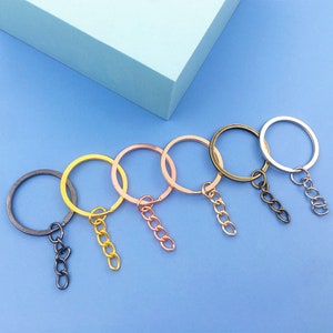 May include: Six key rings with attached chains in different colors: black, gold, rose gold, silver, and bronze. The key rings are all the same size and shape, and the chains are all the same length.