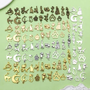 Op de afbeelding: Een grote verzameling zilveren en gouden bedels met katten in verschillende poses. De bedels zijn perfect voor het maken van sieraden, scrapbooking en andere knutselprojecten.