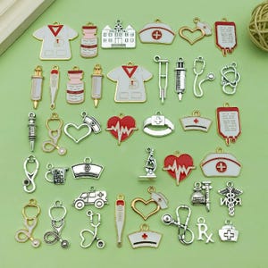 May include: A collection of silver and gold charms with a medical theme. The charms include a stethoscope, a heart, a hospital building, a syringe, a thermometer, a first aid kit, a pill bottle, a microscope, a nurse's hat, a blood bag, a cross, a heart with a heartbeat, a caduceus, and a prescription symbol.