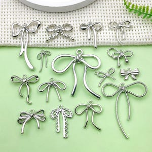 Peut inclure: Une collection de breloques en forme de nœud en métal argenté, parfaites pour la fabrication de bijoux ou les projets d'artisanat. Les nœuds sont disponibles dans une variété de styles, y compris simples, élégants et ornés.