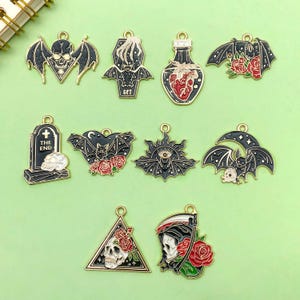 Puede incluir: Conjunto de diez dijes de metal negro y dorado con varios temas de Halloween, incluyendo murciélagos, calaveras, una lápida, una botella de poción, un ataúd y un segador. Los dijes están todos detallados con acentos de esmalte rojo y blanco.