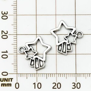 K&ouml;nnte beinhalten: Zwei silberfarbene Stern-Anh&auml;nger. Jeder Anh&auml;nger hat eine gro&szlig;e, offene Sternform mit einem kleineren Stern und einem vertikalen Balkendesign. Die Anh&auml;nger haben eine kleine Schlaufe zum Befestigen.