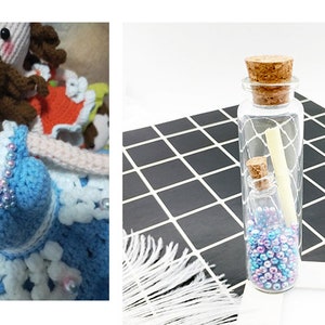 May include: Two glass bottles with cork stoppers filled with iridescent beads and a rolled up piece of paper. The bottles are on a black and white checkered surface.