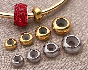 May include: Jewellery beads in gold and silver. A red crystal bead is attached to a gold bracelet. The beads are round with a hole through the centre. The beads are for jewellery making.