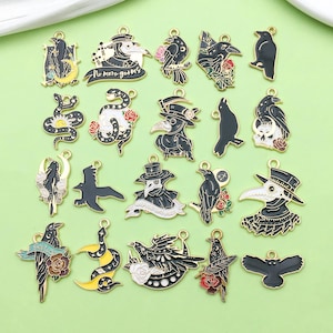 Könnte beinhalten: Ein Set mit 20 goldfarbenen Metall-Anhängern mit verschiedenen schwarzen und weißen Designs. Die Anhänger umfassen einen Pestarzt, eine Schlange, einen zunehmenden Mond, eine Krähe und einen Schädel. Die Anhänger sind perfekt, um Schmuck, Taschen oder anderen Bastelarbeiten eine gotische Note zu verleihen.