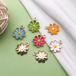 May include: Seven different flower charms with gold metal settings. The charms are in the shapes of daisies with different colored enamel centers and petals. The colors include green, blue, orange, pink, and white.