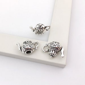 May include: Three silver teapot charms with intricate details. The charms are small and have a vintage look. The charms are perfect for adding a touch of whimsy to jewelry or crafts.