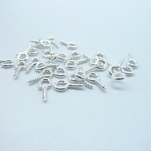 May include: A pile of silver-toned screw-on eye pins, also known as jump rings, for jewelry making.