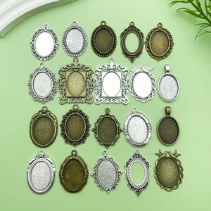 Op de afbeelding: Een verzameling sierlijke, ovaalvormige hangerbakjes in diverse metallic afwerkingen, waaronder zilver, brons en antiek goud. De bakjes hebben decoratieve filigraan en bezel instellingen, perfect voor het maken van aangepaste sieraden of hangers.