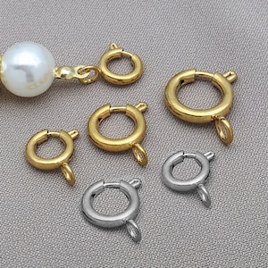 Könnte beinhalten: Eine Auswahl an gold- und silberfarbenen Schmuckverschlüssen. Die Verschlüsse sind rund mit einem Scharnier und einer kleinen Schlaufe zum Befestigen an Schmuck. Eine große weiße Perle ist an einem goldenen Verschluss befestigt.