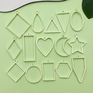 May include: A set of 16 silver-toned metal pendant trays in various shapes, including circles, squares, rectangles, hearts, stars, and more. These trays are perfect for resin crafts and jewelry making.