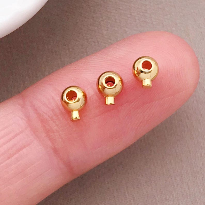 May include: Three gold-colored metal bead caps with a hole in the center. The bead caps are on a finger.