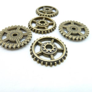 Peut inclure: Cinq engrenages en métal de couleur or antique avec des motifs complexes. Les engrenages sont disposés en demi-cercle sur un fond blanc.