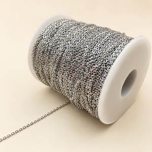 May include: A spool of silver chain, wound around a white plastic spool. The chain is a fine, delicate chain, perfect for jewelry making.