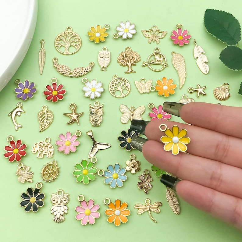 May include: Assortment of gold-tone metal charms with enamel accents. Charms include flowers, animals, trees, and other nature-inspired designs.
