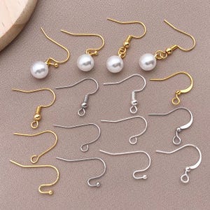 May include: Assortment of gold and silver earring hooks with pearl accents. The hooks are available in a variety of styles, including open loops, closed loops, and jump rings.