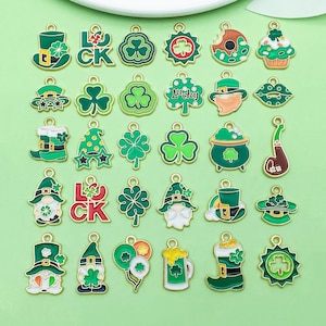 May include: A collection of St. Patrick's Day charms in various shapes, including shamrocks, leprechaun hats, and pots of gold. The charms are primarily green and gold, with some featuring the word "Lucky".