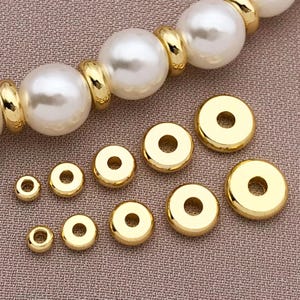 Puede incluir: Un conjunto de cuentas espaciadoras de metal de color dorado en varios tamaños. Las cuentas son redondas con un agujero en el centro.