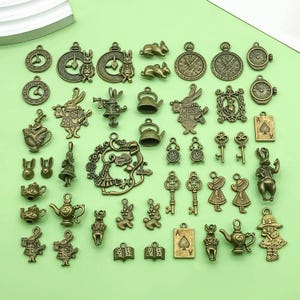 以下が含まれることがあります： アリス・イン・ワンダーランドのキャラクター、トランプ、ティーポット、時計、鍵、ウサギをモチーフにしたアンティークゴールド調の金属製チャーム40個のセットです。