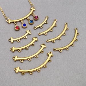 May include: Gold-coloured jewellery components and a necklace with colourful gemstone accents. The components are curved bars with multiple holes for connecting. The necklace has a delicate chain and features red, blue, and pink gemstones.