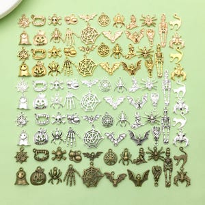 May include: A collection of silver and gold Halloween charm pendants. The charms include bats, spiders, ghosts, pumpkins, skulls, and more.