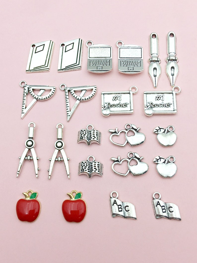 May include: A collection of silver charm pendants with school-themed designs, including books, apples, a protractor, a compass, a laptop, a pen, and a heart with an apple. The charms are perfect for adding a touch of school spirit to jewelry or crafts.