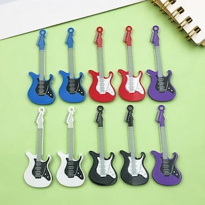 Puede incluir: Una colección de miniaturas de guitarras eléctricas en varios colores, incluyendo azul, rojo, blanco, negro y morado. Cada guitarra tiene un golpeador y clavijero contrastantes, con cuerdas y trastes plateados. Las guitarras están dispuestas sobre una superficie verde.