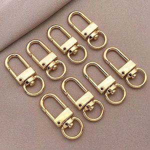 May include: A set of ten gold-toned metal key rings with a swivel clasp. The key rings are all the same size and shape, and they are arranged in a circle.