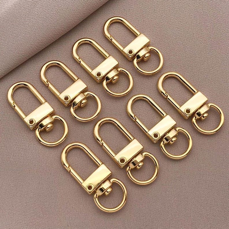 May include: A set of ten gold-toned metal key rings with a swivel clasp. The key rings are all the same size and shape, and they are arranged in a circle.