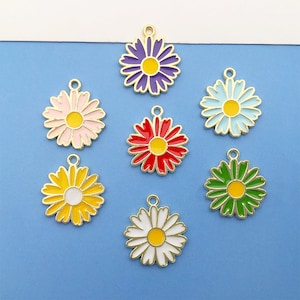 Op de afbeelding: Zeven goudkleurige metalen madeliefjescharms met emaille verf in verschillende kleuren: paars, roze, rood, groen, blauw, geel en wit.