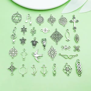 Può includere: Una collezione di connettori e ciondoli per gioielli in metallo color argento con varie forme, tra cui una Stella di David, note musicali, una croce, una tartaruga, una farfalla, un uccello, un'ancora, una luna crescente e un simbolo di infinito.