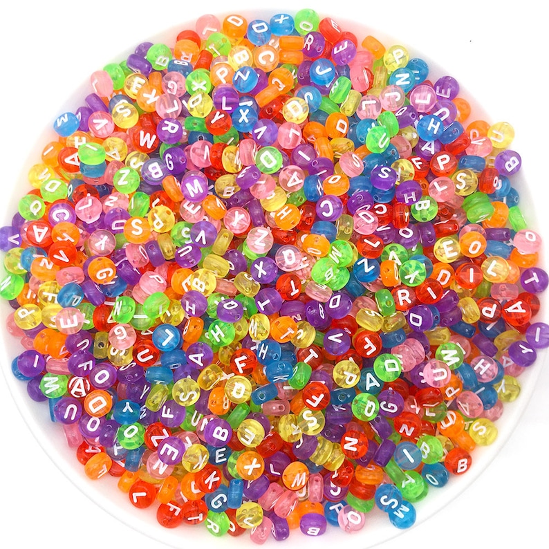 May include: A bowl filled with colorful alphabet beads. The beads are translucent and have white letters on them. The beads are a mix of colors, including red, orange, yellow, green, blue, purple, and pink.