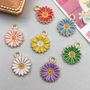 Könnte beinhalten: Sechs goldfarbene Metall-Gänseblümchen-Anhänger mit emaillierten Blütenzentren. Die Anhänger sind in Pink, Rot, Gelb, Blau, Grün und Lila.