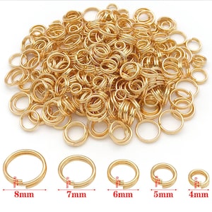 Op de afbeelding: Een verzameling goudkleurige splitringen in verschillende maten, variërend van 4 mm tot 8 mm in diameter. De afbeelding toont een grote stapel ringen, met verschillende individuele ringen om de verschillende maten te laten zien. Deze ringen worden gebruikt bij het maken van sieraden en knutselen.