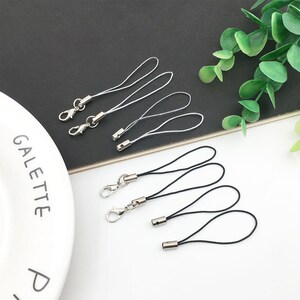 Op de afbeelding: Een set zilveren sleutelhangers met zwarte en witte koorden. De sleutelhangers hebben een zilveren lus en een zilveren ring.