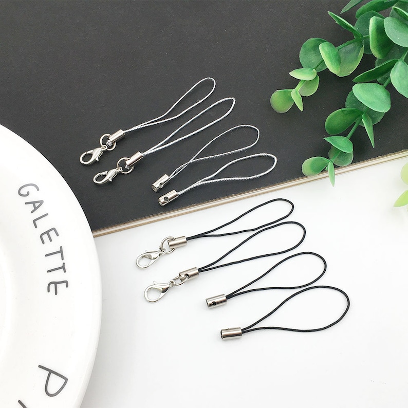Op de afbeelding: Een set zilveren sleutelhangers met zwarte en witte koorden. De sleutelhangers hebben een zilveren lus en een zilveren ring.