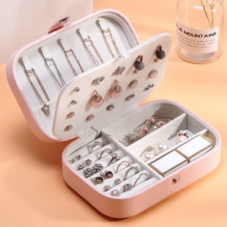 May include: A pink velvet jewellery box with a hinged lid. The box has multiple compartments for storing earrings, rings, necklaces, and other jewellery. The box is open and the compartments are filled with various pieces of jewellery.