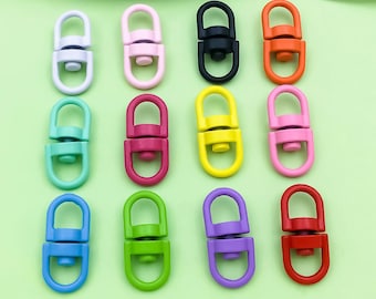 Puede incluir: Una colección de cierres giratorios coloridos en varios tonos, incluyendo blanco, rosa, negro, naranja, verde azulado, burdeos, amarillo, rosa claro, azul, verde, morado y rojo. Los cierres están dispuestos sobre una superficie verde claro.
