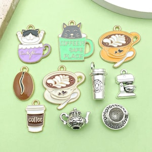 Könnte beinhalten: Sortiment von 10 goldenen und silbernen Anhänger-Anhängern mit Kaffee- und Katzenthemen. Die Anhänger umfassen eine Kaffeetasse mit einem Katzenkopf, eine Kaffeetasse mit dem Text "Coffee is Safe Place", eine Kaffeetasse mit Latte-Design, eine Kaffeebohne, eine Kaffeetasse, eine Kaffeemaschine, eine Teekanne, eine Untertasse und eine To-Go-Kaffeetasse.