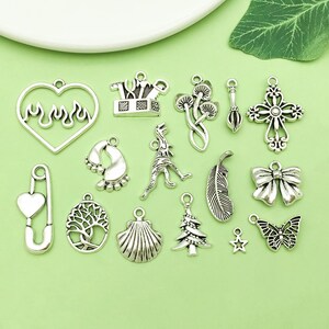 Peut inclure: Collection de breloques argentées de formes variées : cœur enflammé, épingle à nourrice cœur, arbre, coquillage, sapin, étoile, papillon, croix et nœud papillon.