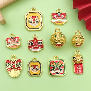 May include: A collection of gold-colored metal charms with red, yellow, and green accents. The charms feature various designs, including lion dance masks and traditional Chinese motifs. Some charms have the Chinese characters for "blessing".