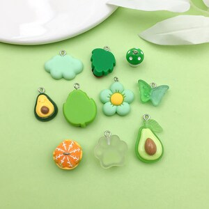 Puede incluir: Surtido de colgantes de charms verdes y amarillos, que incluyen una nube, una hoja, una flor, una mariposa, un aguacate y una naranja. Los charms est&aacute;n hechos de arcilla polim&eacute;rica y tienen un acabado brillante.