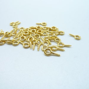 May include: A pile of gold-colored screw-in eyelet hooks. The hooks have a small loop at the top and a screw-in base.